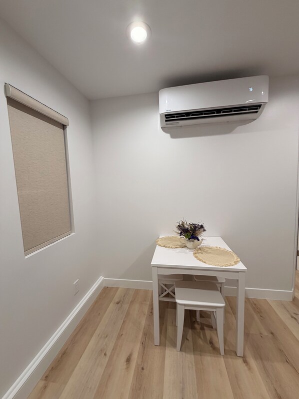 Una stanza piccola con un tavolo bianco, una panca, una lampada a soffitto e un condizionatore d'aria a parete.