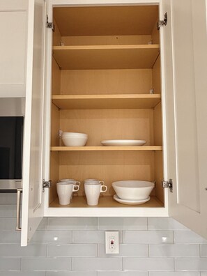 Ein offenes Schrank mit Regalen, gefüllt mit weißen Schüsseln und Tassen.