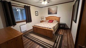 A bedroom with a wooden bed, a ceiling fan, a window with curtains, a radiator, and a rug.