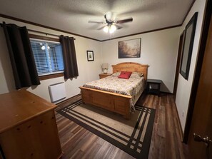 A bedroom with a wooden bed, a ceiling fan, a window with curtains, a radiator, and a rug.