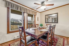 A dining room with a wooden table, six chairs, a ceiling fan, and large windows. - Beech Mountain Condo | Pool, Hot Tub + Fireplace (Beech Mountain)