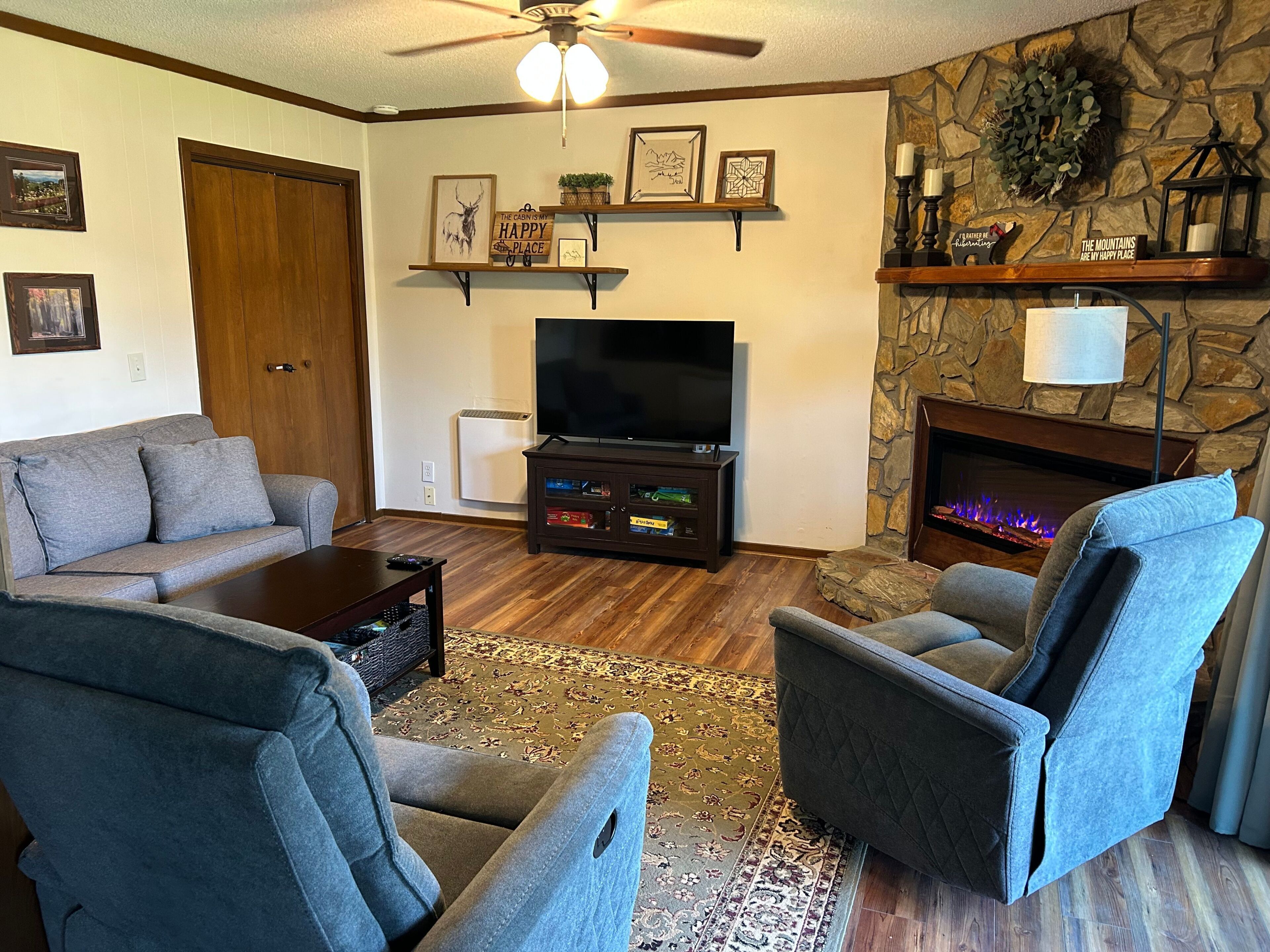 A living room with a sofa, two armchairs, a TV, a fireplace, and decorative wall shelves.