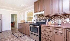 A kitchen with brown cabinets, a stainless steel oven, and a tiled backsplash. - Tranquil Riverfront Retreat (Depauw)
