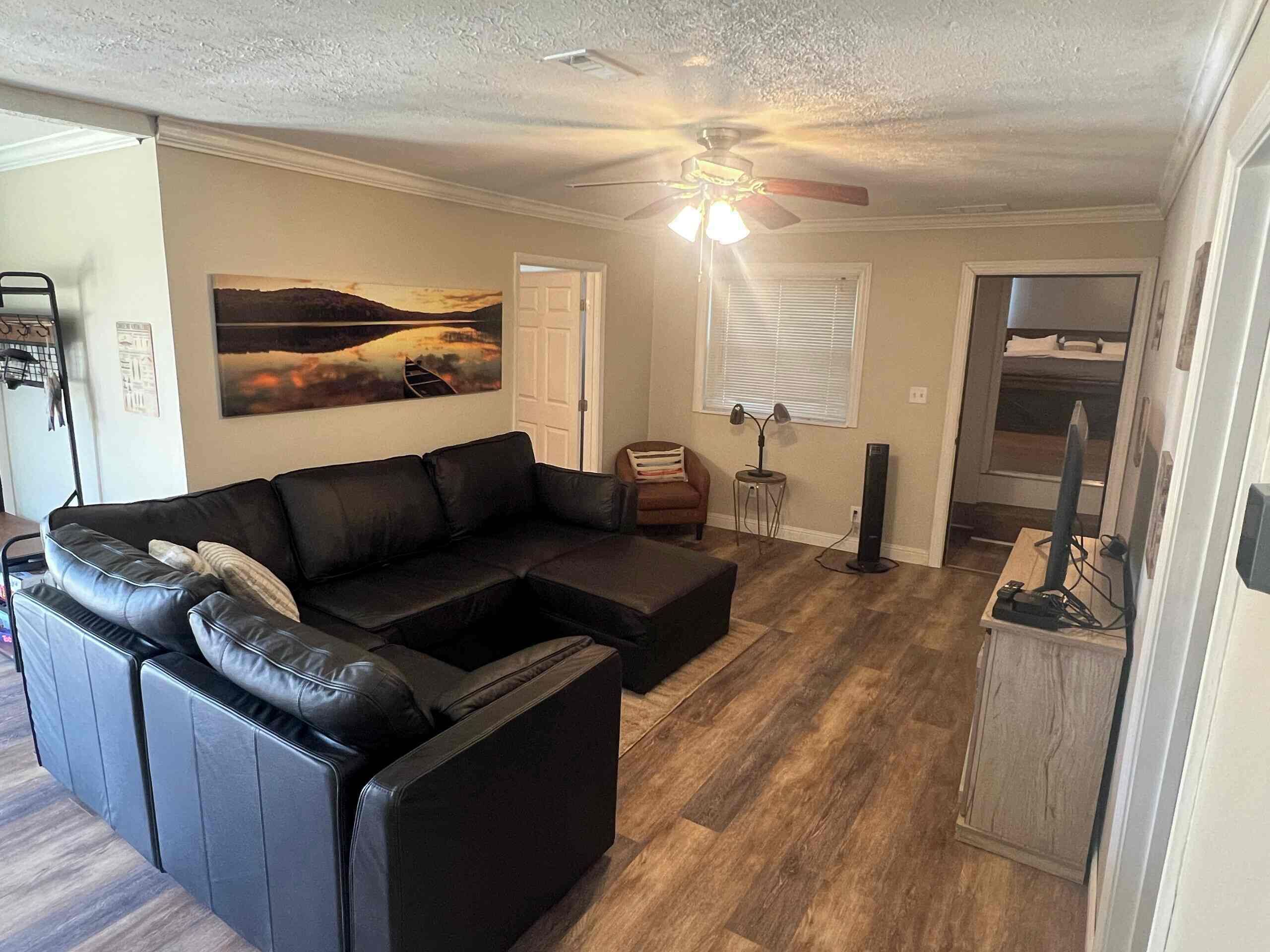 A living room with a sectional sofa, a ceiling fan, a painting, and a computer desk.