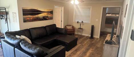 A living room with a sectional sofa, a ceiling fan, a painting, and a computer desk.
