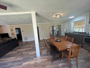 A dining area with a wooden table and chairs, a kitchen with a refrigerator and stove, and a living room with a sofa and television. - Tranquil Riverfront Retreat (Depauw)