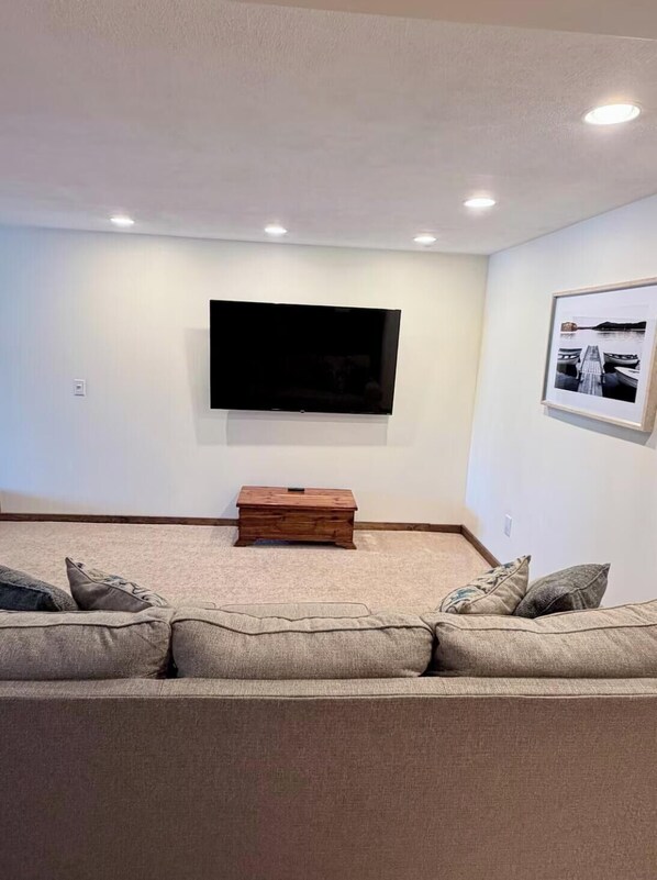 A living room with a flat-screen TV mounted on the wall, a wooden coffee table, and a beige sofa with cushions. - Beautiful Lakefront Property (Alpine)