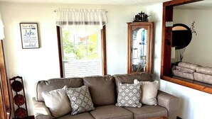 A living room with a brown sofa, patterned cushions, a wooden coffee table, a mirror, and a window with a view.
