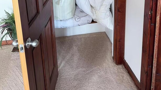 A room with a wooden door, a closet with hanging clothes, and a bed with white bedding.