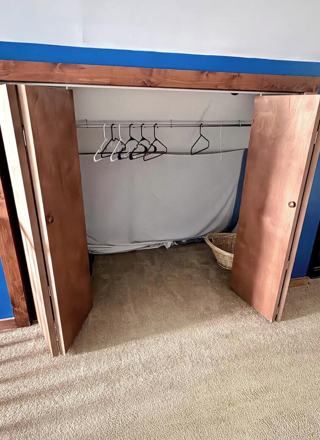 Een kamer met een houten deur die leidt naar een inloopkast met een kledingroede en een mand.