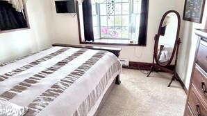 A bedroom with a bed, a dresser, a mirror, a window with curtains, and a ceiling light fixture.
