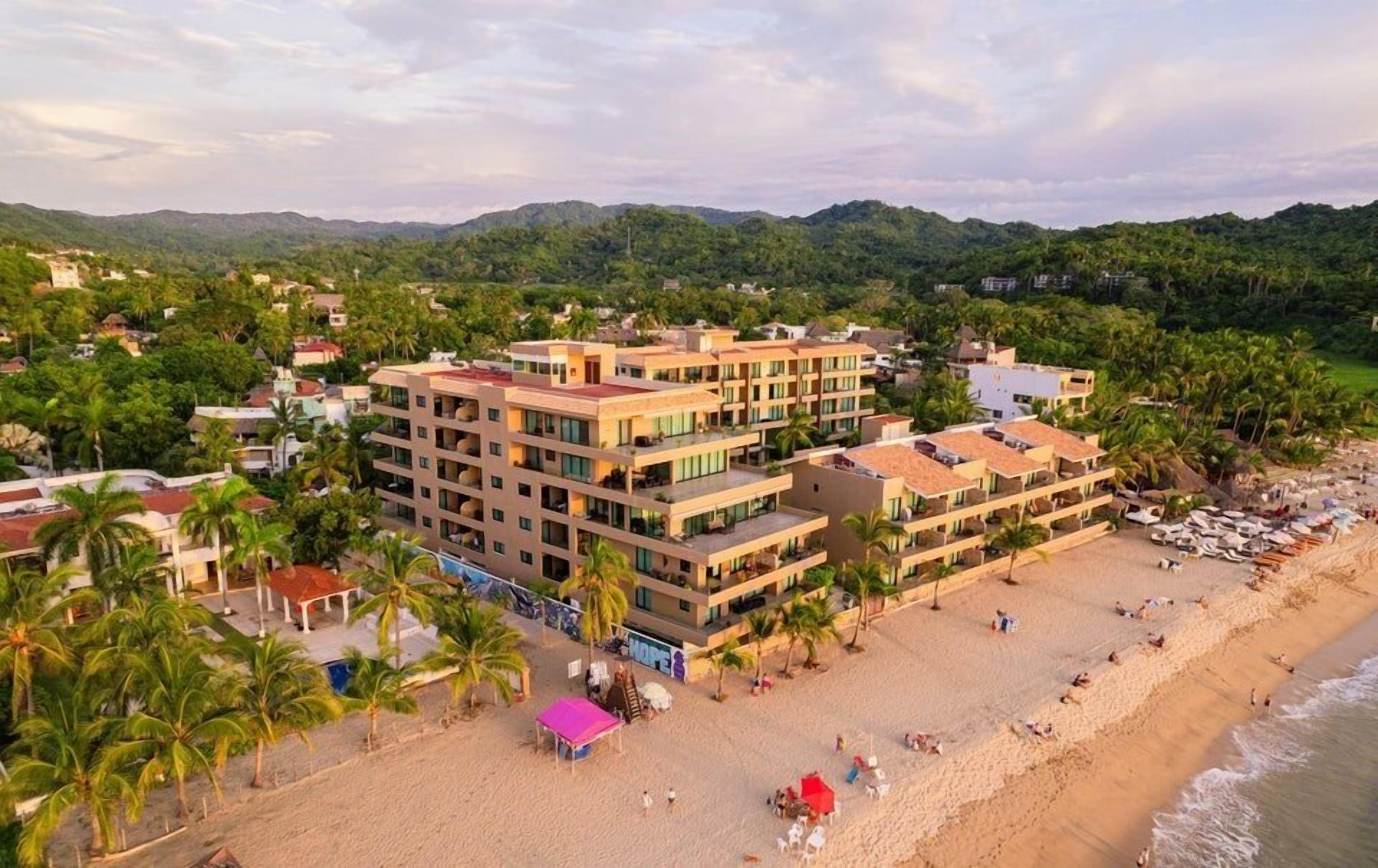 A multi-story hotel with a beachside location, featuring a pool area and a beach with umbrellas.