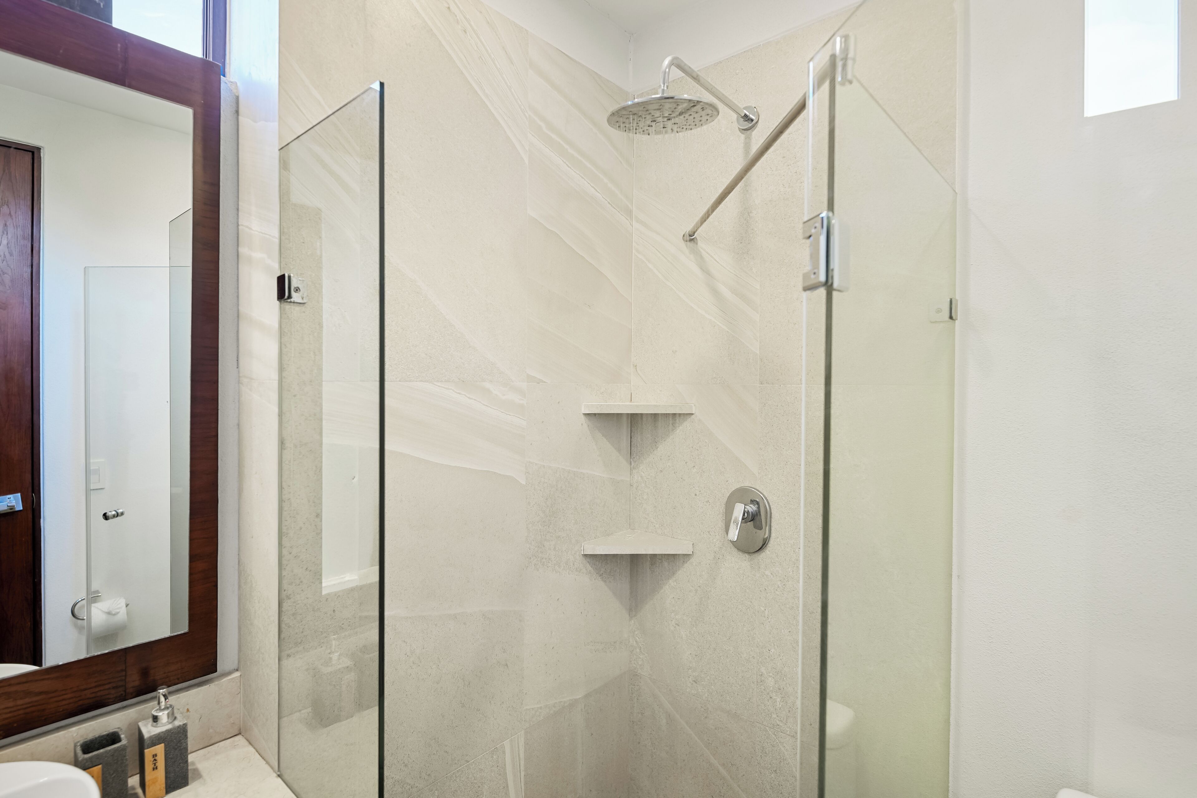 Une salle de bain moderne avec une douche à parois de verre, un grand miroir et un mur en marbre.