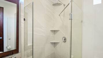 Une salle de bain moderne avec une douche à parois de verre, un grand miroir et un mur en marbre.