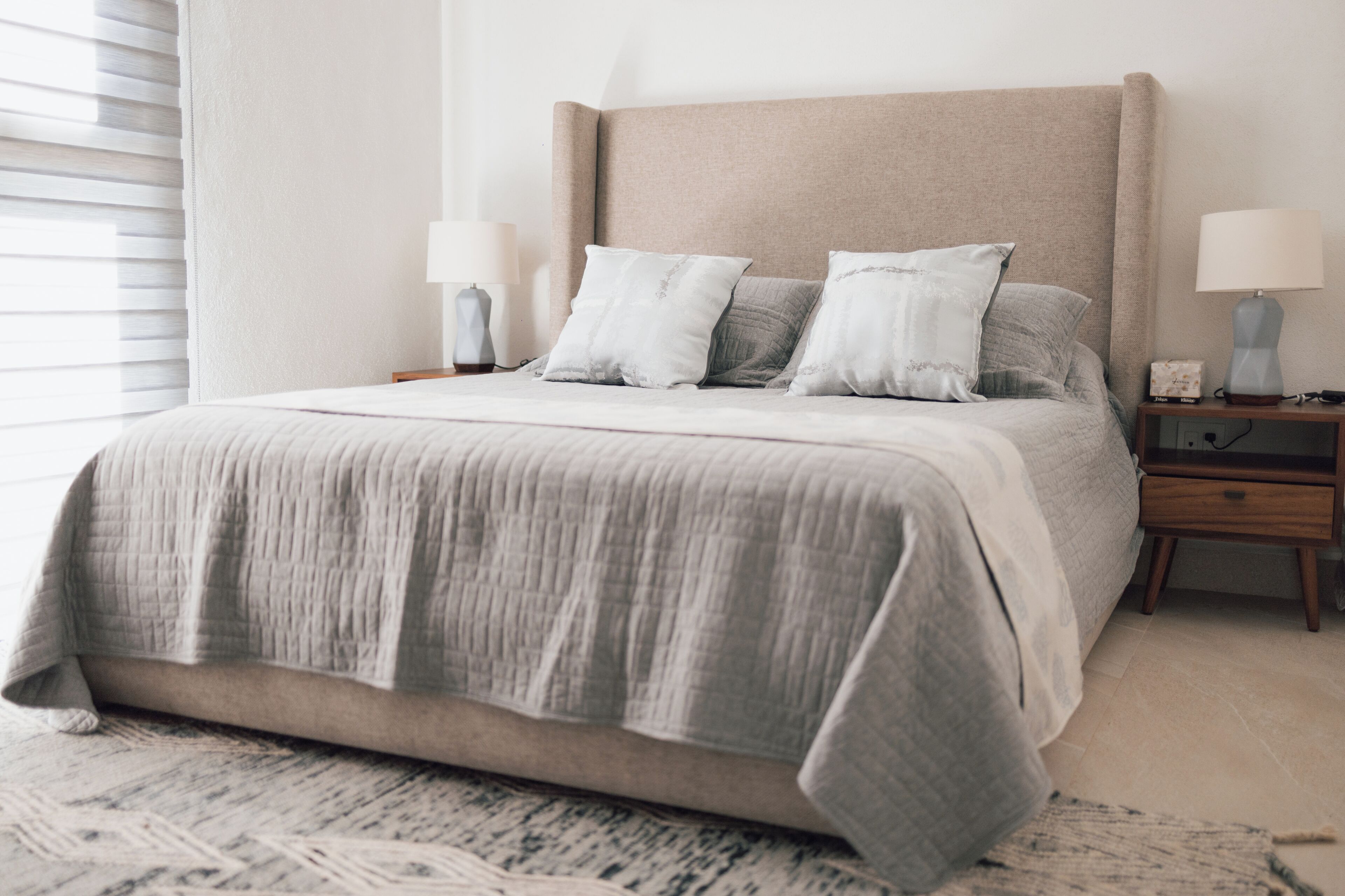 A bed with a grey quilt, two bedside tables with lamps, and a patterned rug.