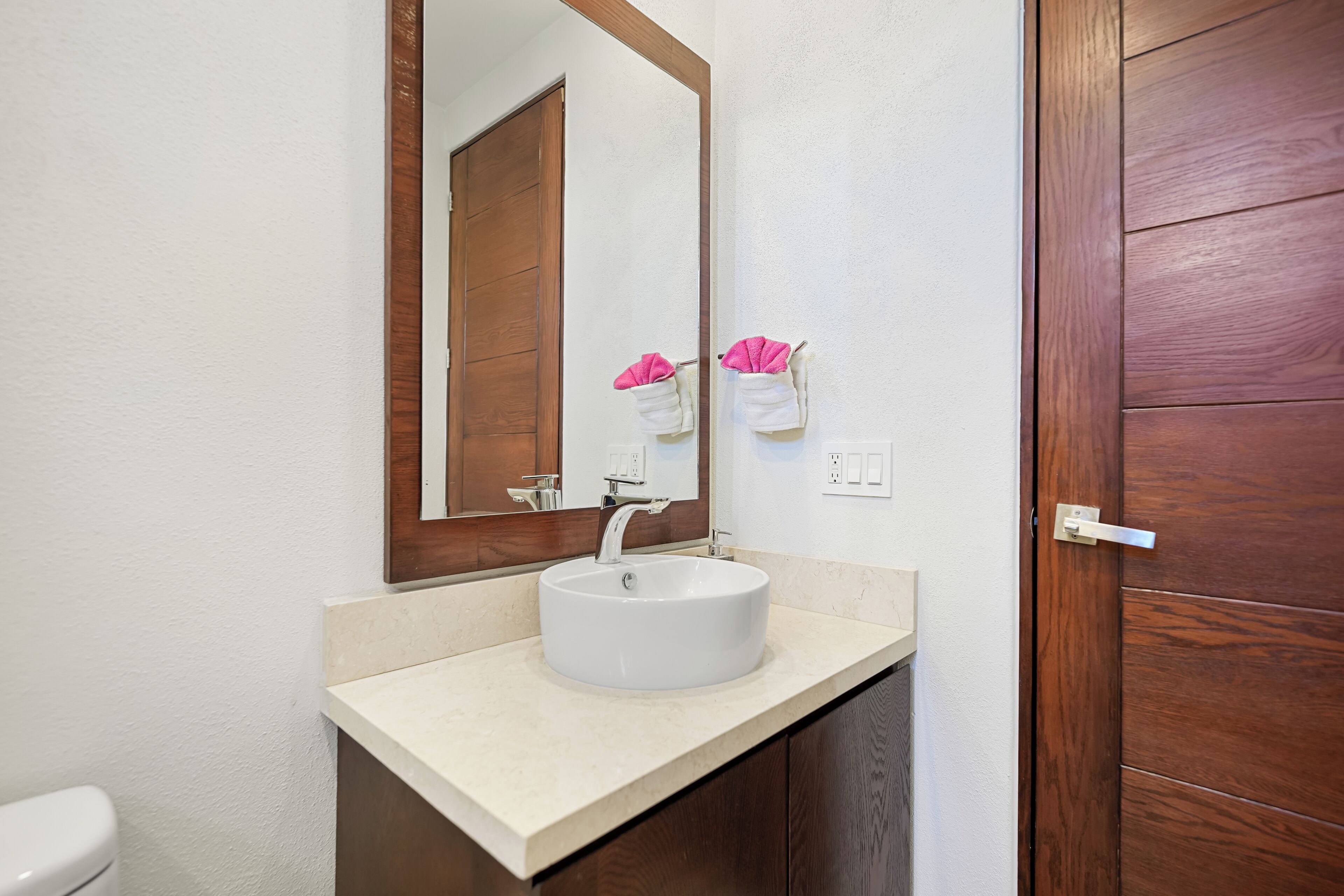 Un baño con un lavamanos blanco, un espejo y una puerta de madera.