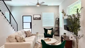 Una sala de estar moderna con un sofá, un sillón verde, una mesa de centro, un televisor y una escalera.