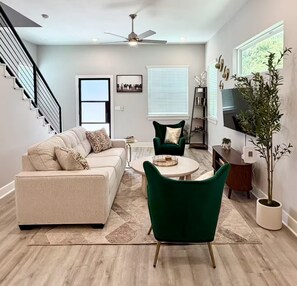 Ein modernes Wohnzimmer mit einer Couch, einem grünen Sessel, einem Couchtisch, einem Fernseher und einer Treppe.