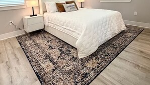 Un dormitorio con cama, mesitas de noche, alfombra y ventilador de techo.