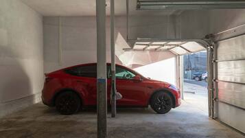 Un auto rojo estacionado dentro de un garaje con puerta metálica y piso de concreto.