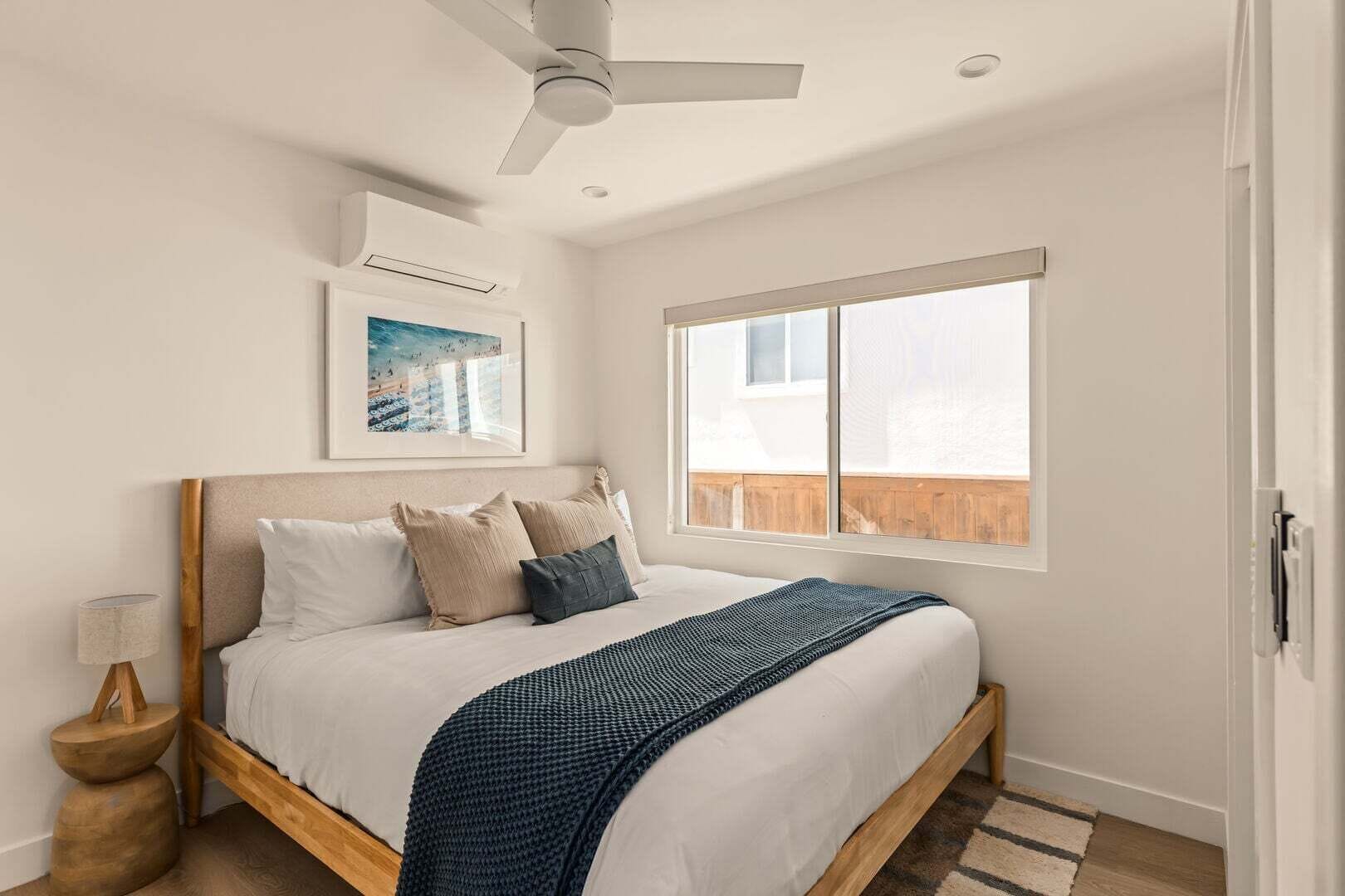Un dormitorio con una cama, ventilador de techo, ventana y aire acondicionado de pared.