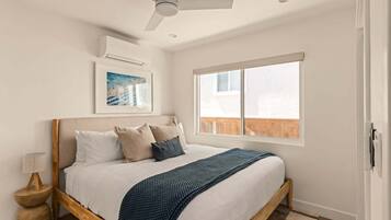 Un dormitorio con una cama, ventilador de techo, ventana y aire acondicionado de pared.