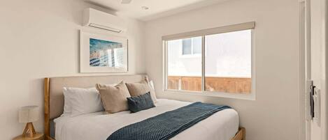 Un dormitorio con una cama, ventilador de techo, ventana y aire acondicionado de pared.