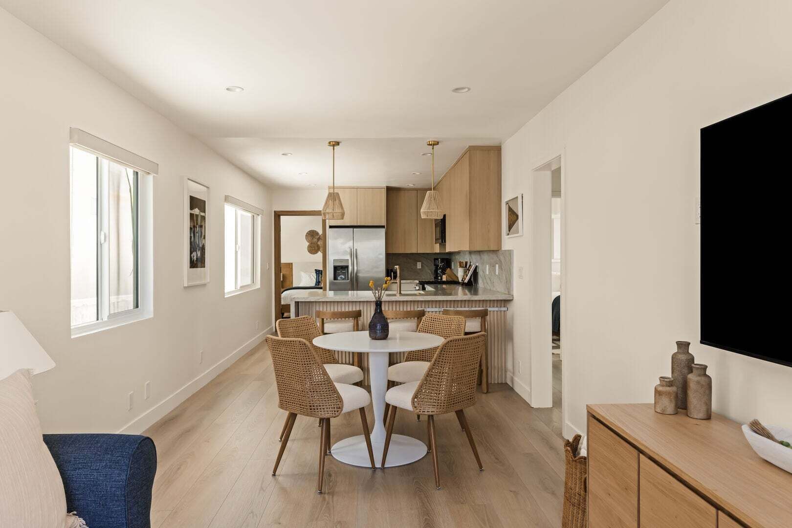 A modern kitchen with a central island, dining area with wicker chairs, and a flat-screen TV mounted on the wall.