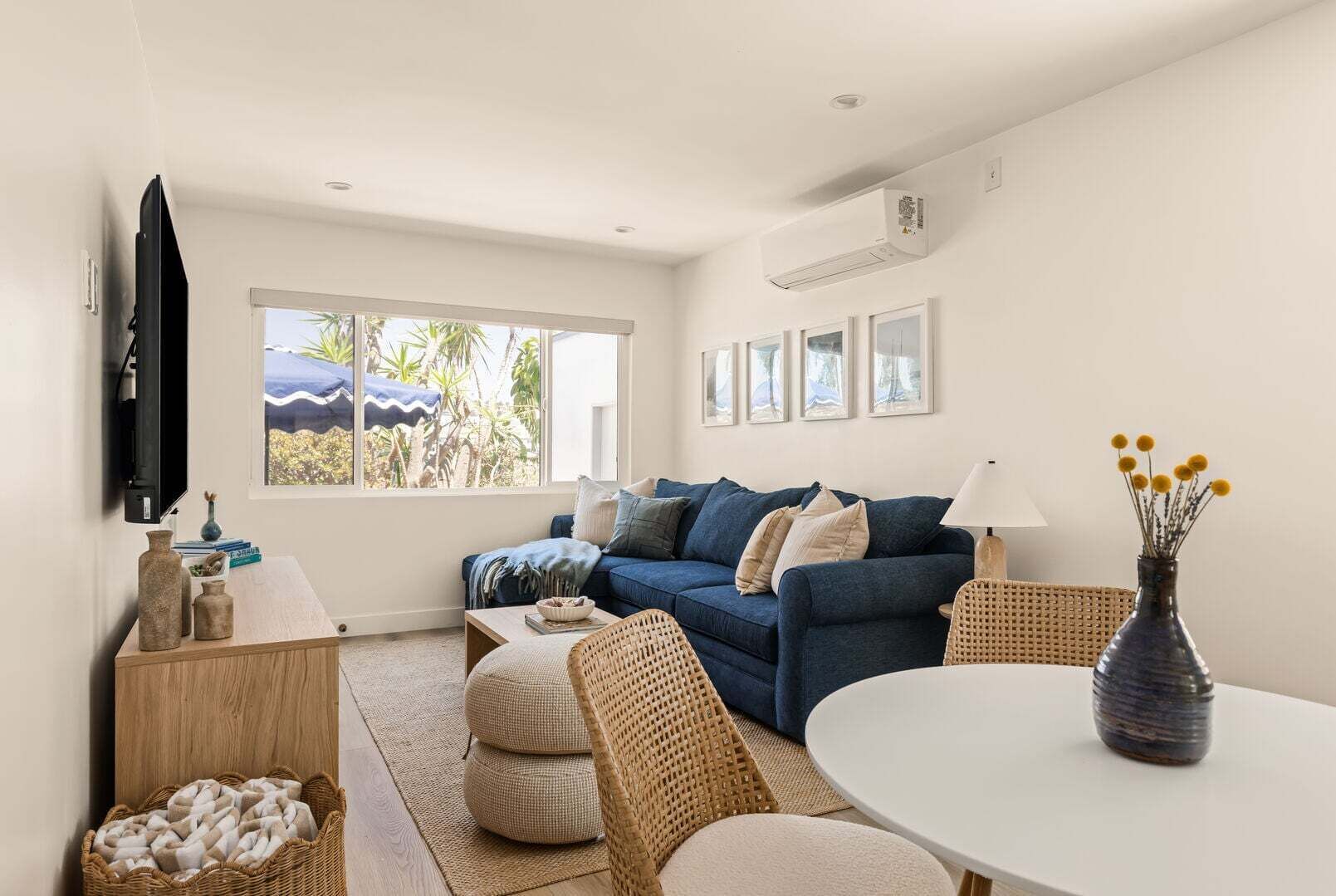 A modern living room with a blue sofa, a TV mounted on the wall, and a dining area with a table and chairs.