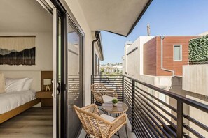 A balcony with a bed, a table, and chairs, overlooking a cityscape.