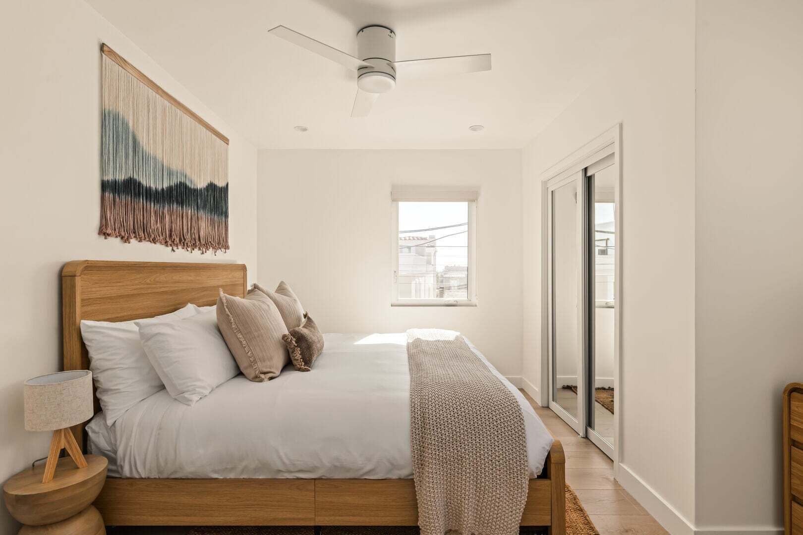 Une chambre à coucher avec un lit, des oreillers, une lampe de chevet, un ventilateur de plafond et une vue par la fenêtre.