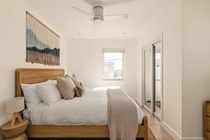 A bedroom with a bed, pillows, a bedside lamp, a ceiling fan, and a view through a window.