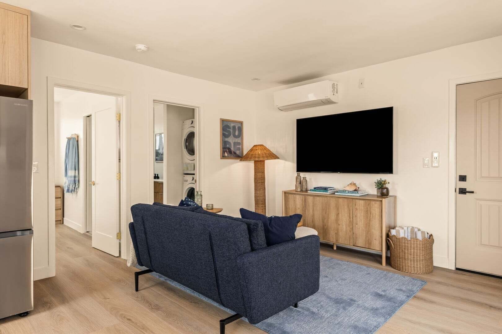 Una sala moderna con un sofá, un televisor de pantalla plana, una lámpara y una lavadora al fondo.