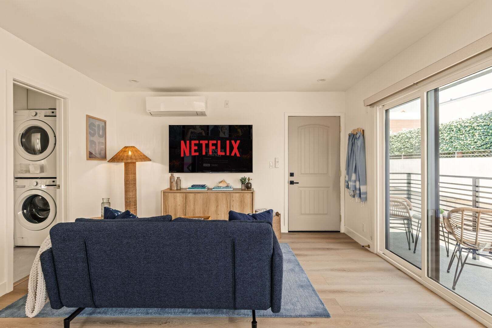 Un salon moderne doté d’un grand téléviseur à écran plat, d’un canapé, d’un lave-linge et d’une porte-fenêtre coulissante donnant sur un balcon.