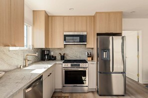 Eine moderne Küche mit Holzausstattung, einem Edelstahlkühlschrank, einem eingebauten Backofen und einer Mikrowelle.