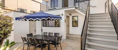 Un patio con una mesa y sillas, una sombrilla, una escalera y un edificio con balcón.