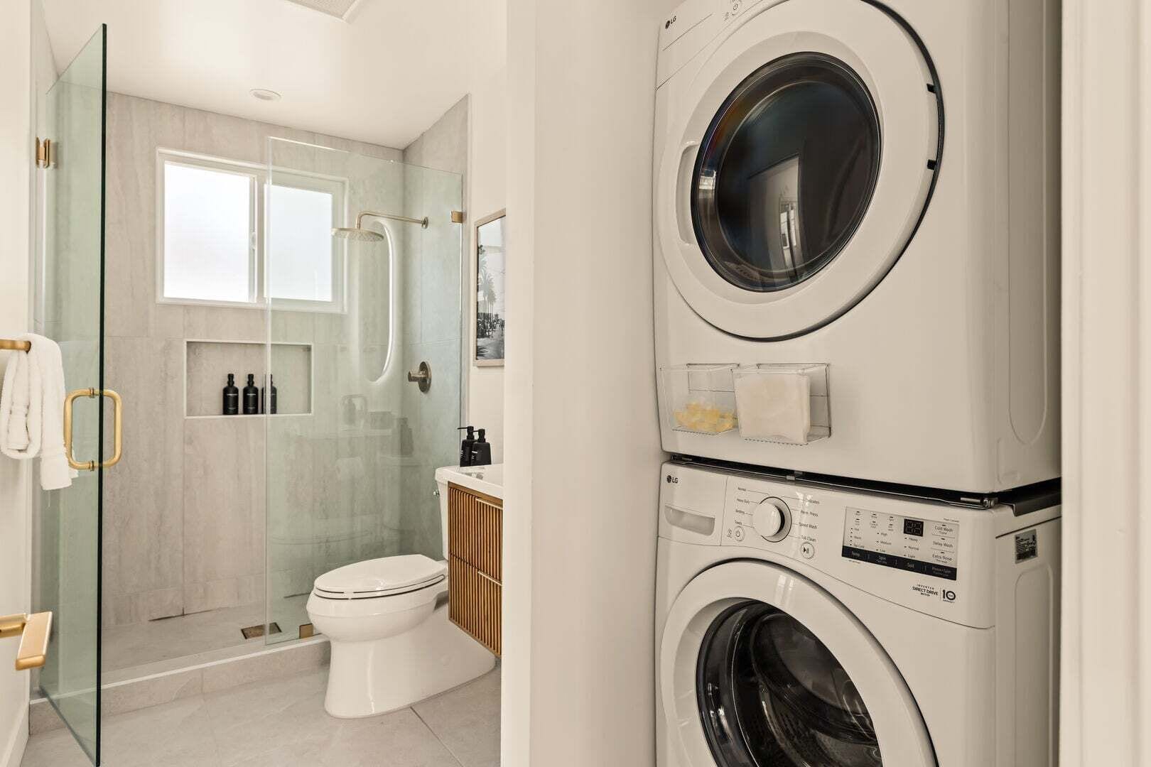 A modern bathroom with a glass shower enclosure, a toilet, and a stacked washer and dryer unit.