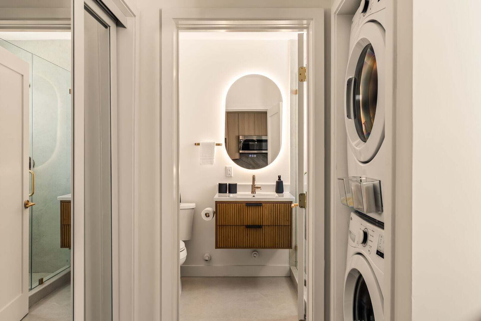 A modern bathroom with a toilet, sink, mirror, and a washing machine.