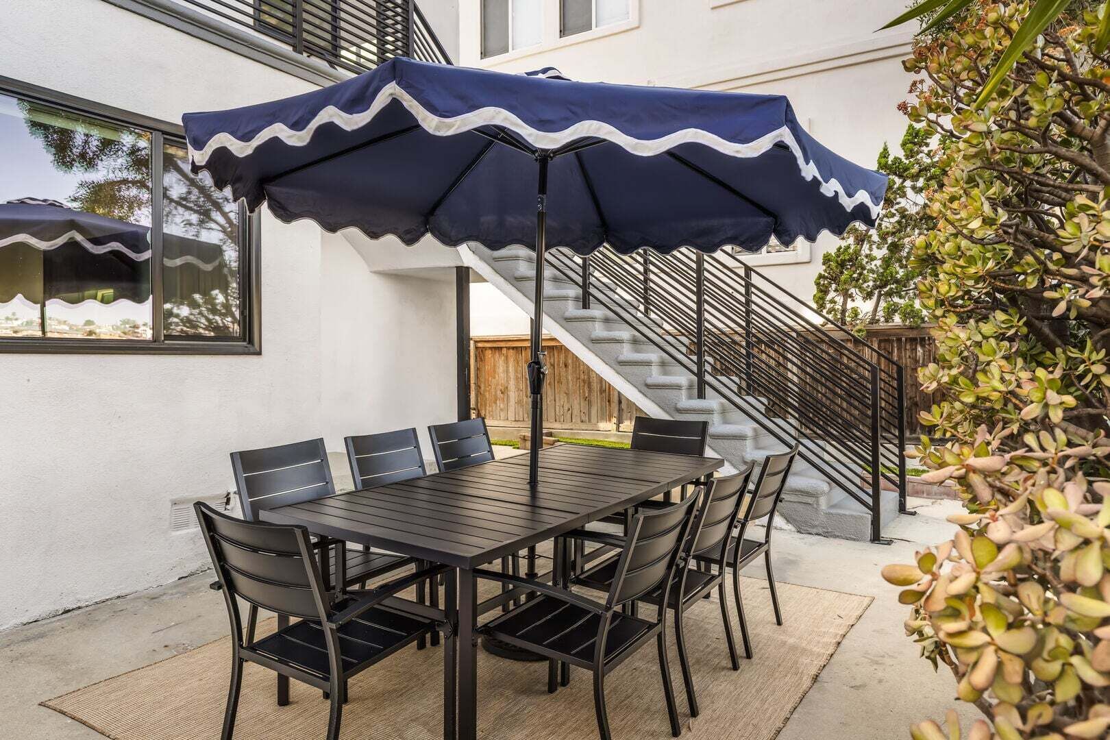Un patio exterior con una mesa, sillas, un paraguas azul y una escalera.