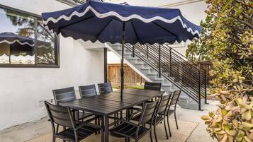 Un patio exterior con una mesa, sillas, un paraguas azul y una escalera.