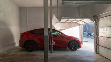A red car parked inside a garage with a metal door and concrete floor.
