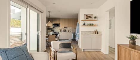 Un interior moderno con sofá, sillones, zona de comedor, cocina y televisor.