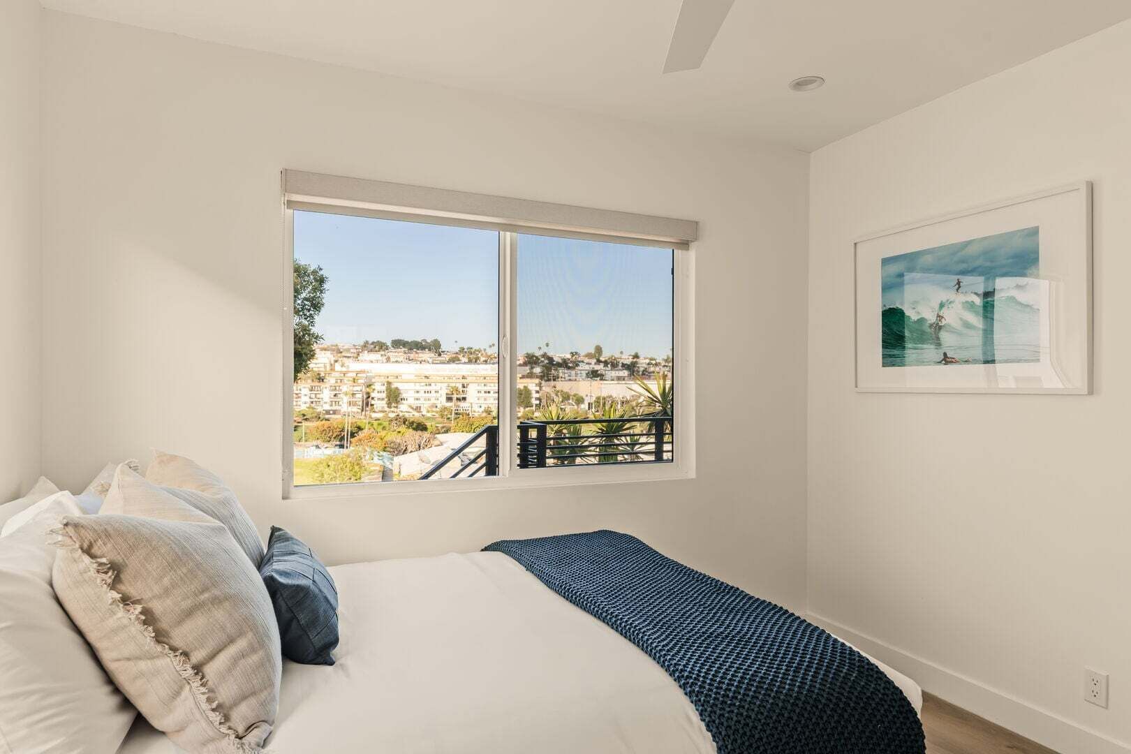 Ein Schlafzimmer mit einem großen Fenster, einem Bett und einem gerahmten Bild an der Wand.