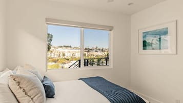 Ein Schlafzimmer mit einem großen Fenster, einem Bett und einem gerahmten Bild an der Wand.