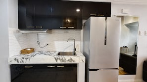A modern kitchen with a stainless steel refrigerator, black cabinets, and a marble countertop. - Mercado Presidential Suite (Makati City)