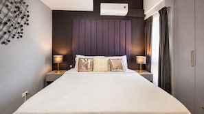 A modern hotel room with a large bed, two bedside tables with lamps, a wall-mounted air conditioner, and a window with curtains. - Mercado Presidential Suite (Makati City)