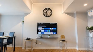 A modern living room with a flat-screen TV mounted on the wall, a round clock above it, and a dining area with a table and chairs. - Mercado Presidential Suite (Makati City)