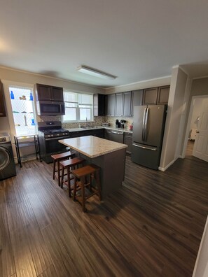A modern kitchen with a central island, stainless steel appliances, and wooden flooring. - The Hideaway Walk to Falls W/D Sleeps 8 (Niagara Falls)