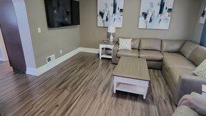 A living room with a sectional sofa, a coffee table, a TV mounted on the wall, and abstract art pieces. - The Hideaway Walk to Falls W/D Sleeps 8 (Niagara Falls)
