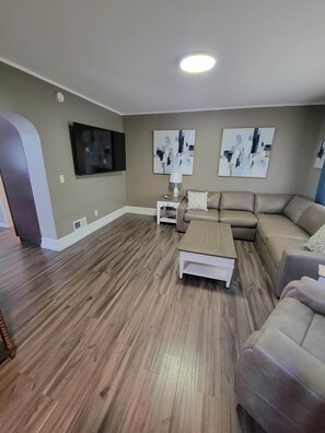 A living room with a sectional sofa, a coffee table, a TV mounted on the wall, and abstract art pieces. - The Hideaway Walk to Falls W/D Sleeps 8 (Niagara Falls)